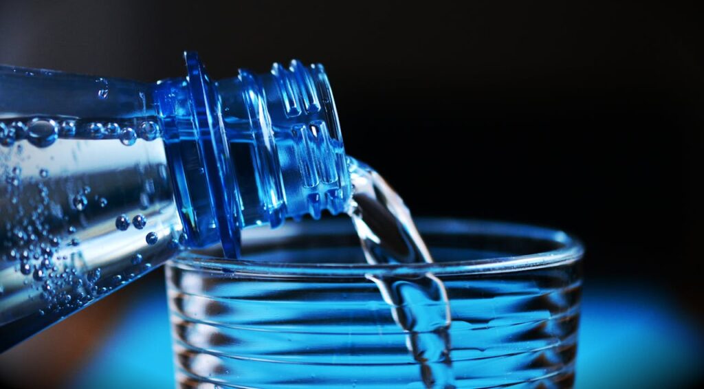 Wasser aus Flasche wird in Glas eingeschenkt